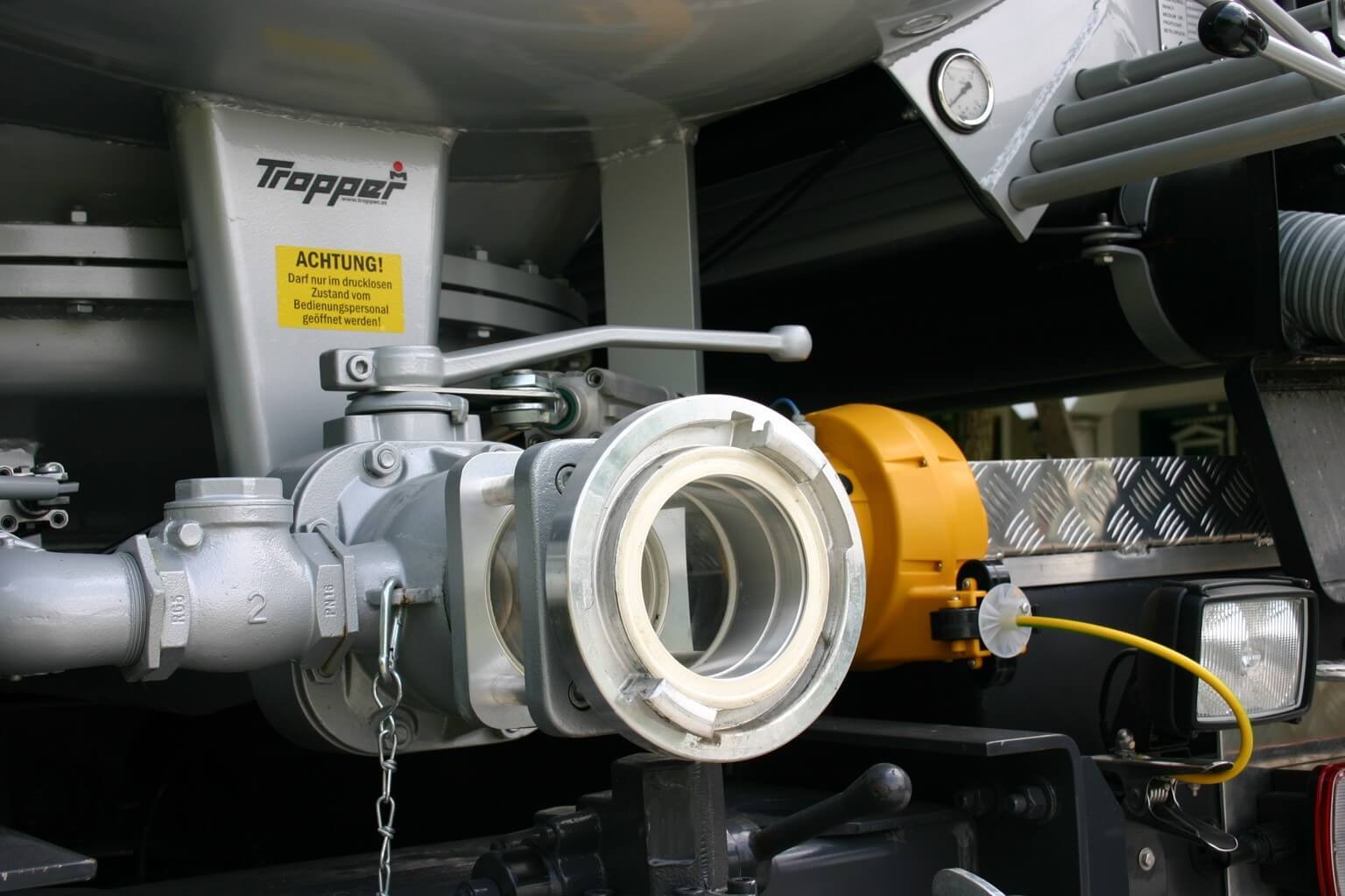 Ventil und Armatur eines industriellen Tanks mit gelber Sicherheitswarnung, Nahaufnahme technischer Details.